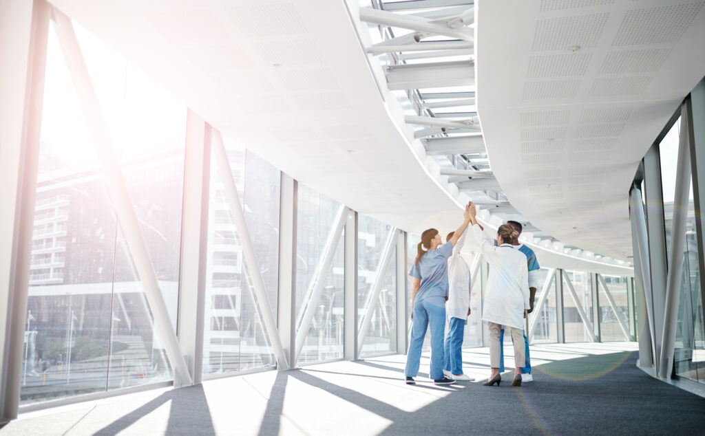 A group of nurses and doctors in a sunlit corridor high-fiving each other.