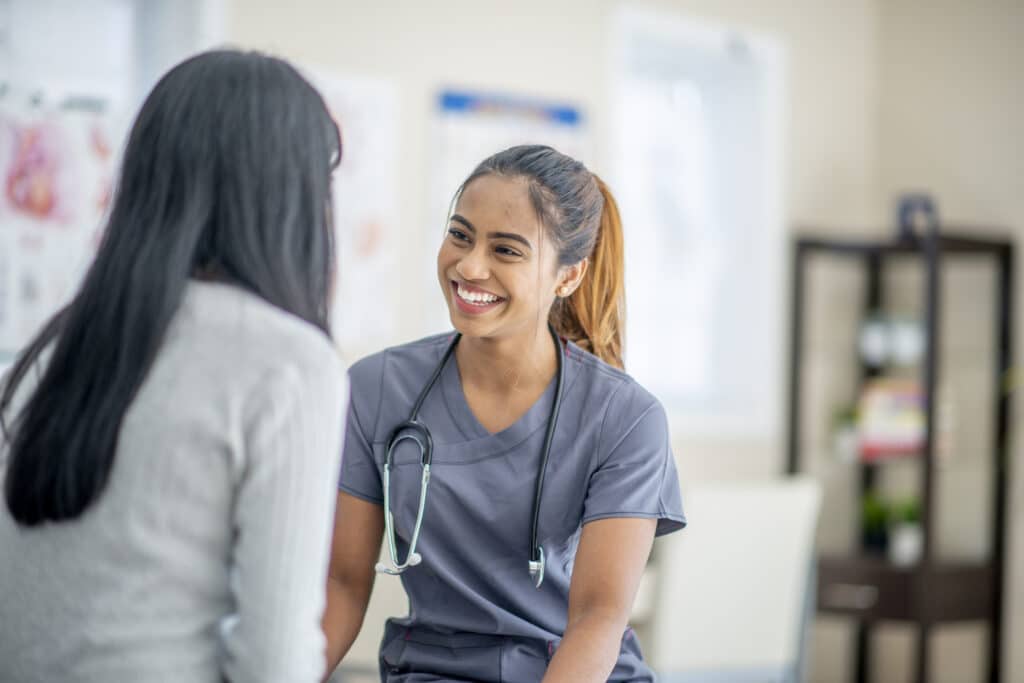 young female nurse smiling widely at her patient who is sitting across her in an office